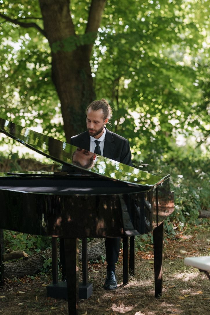 Arian M&uuml;ller playing grand piano among the trees